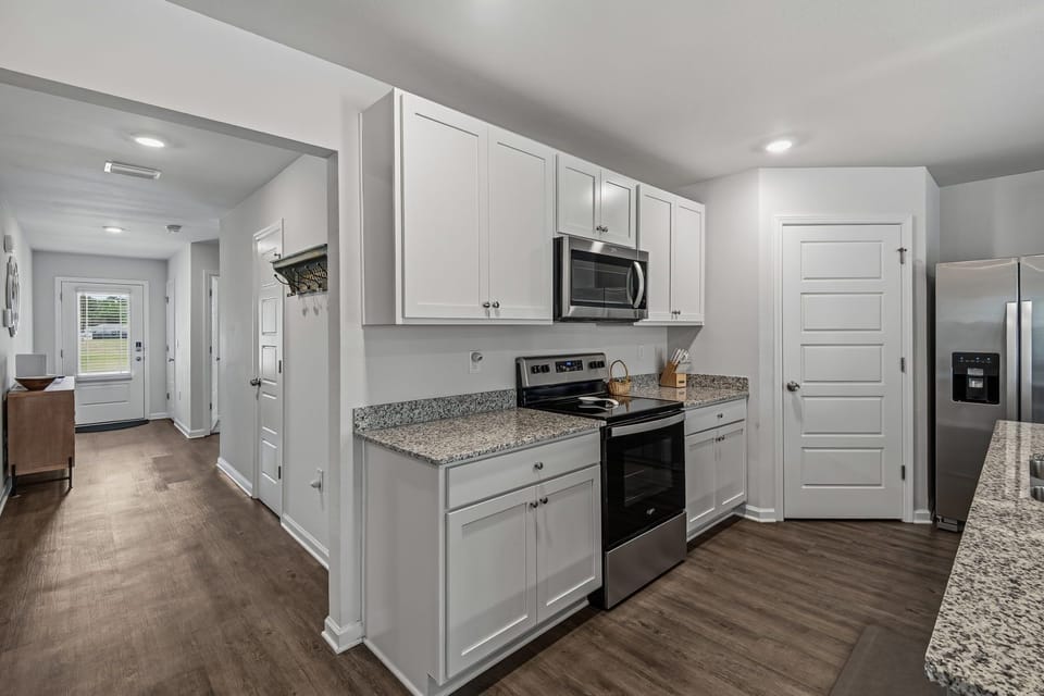 Kitchen with white cabinets, dark granite counters, stainless microwave and oven — entryway with coat rack behind