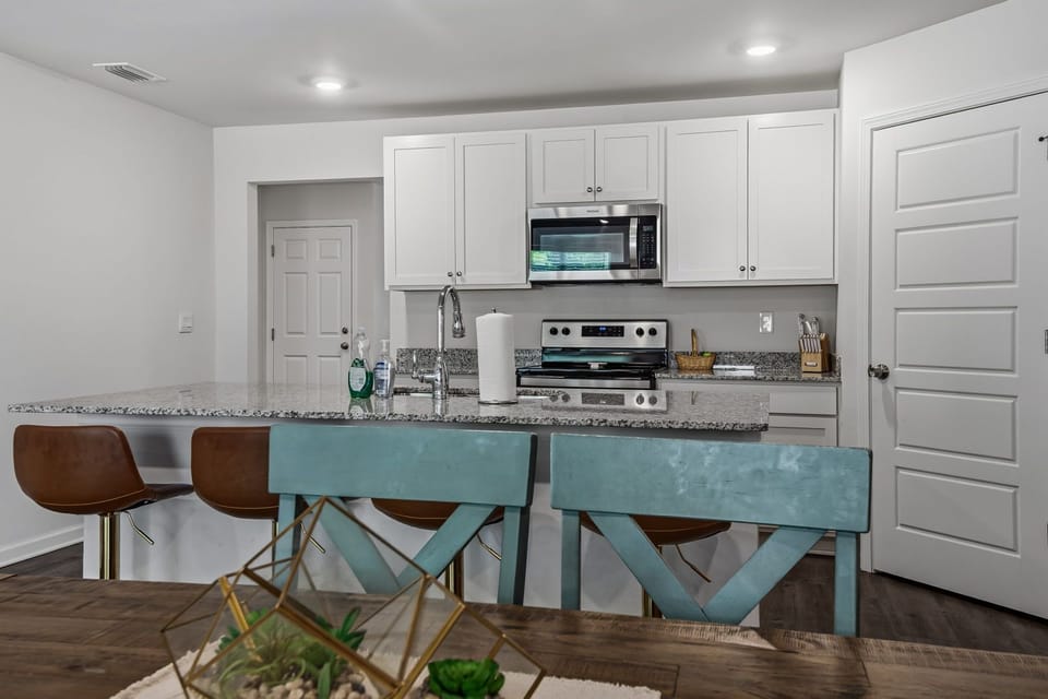 Kitchen island with granite countertop and two brown bar stools — teal dining chair visible in the background