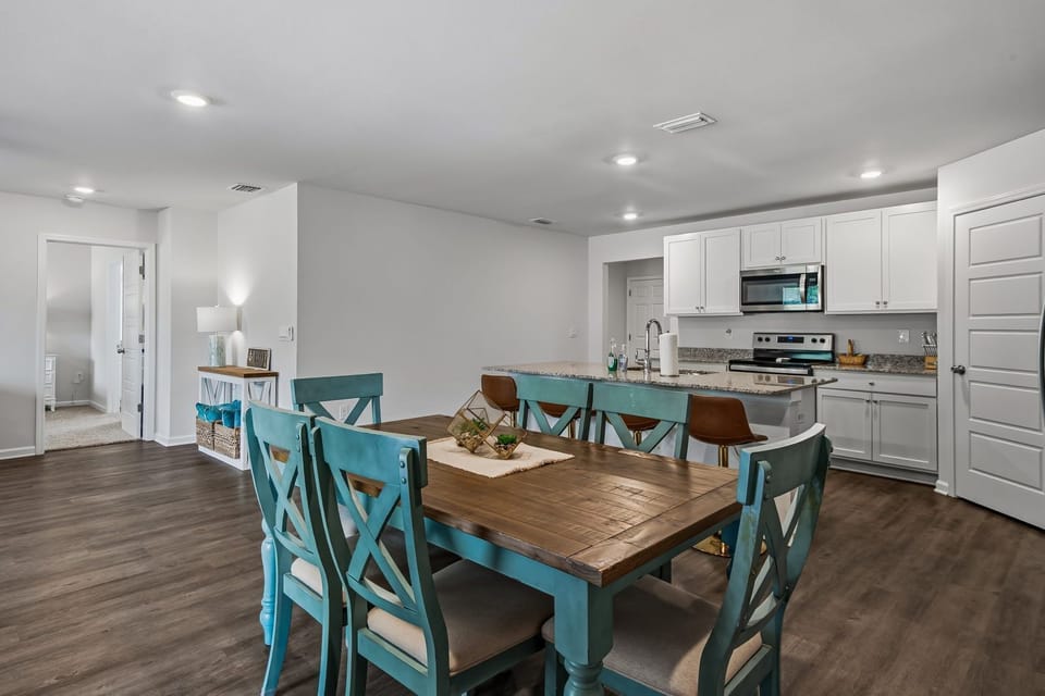 Dark wood dining table with six turquoise chairs, open to the kitchen with white cabinets and stainless appliances