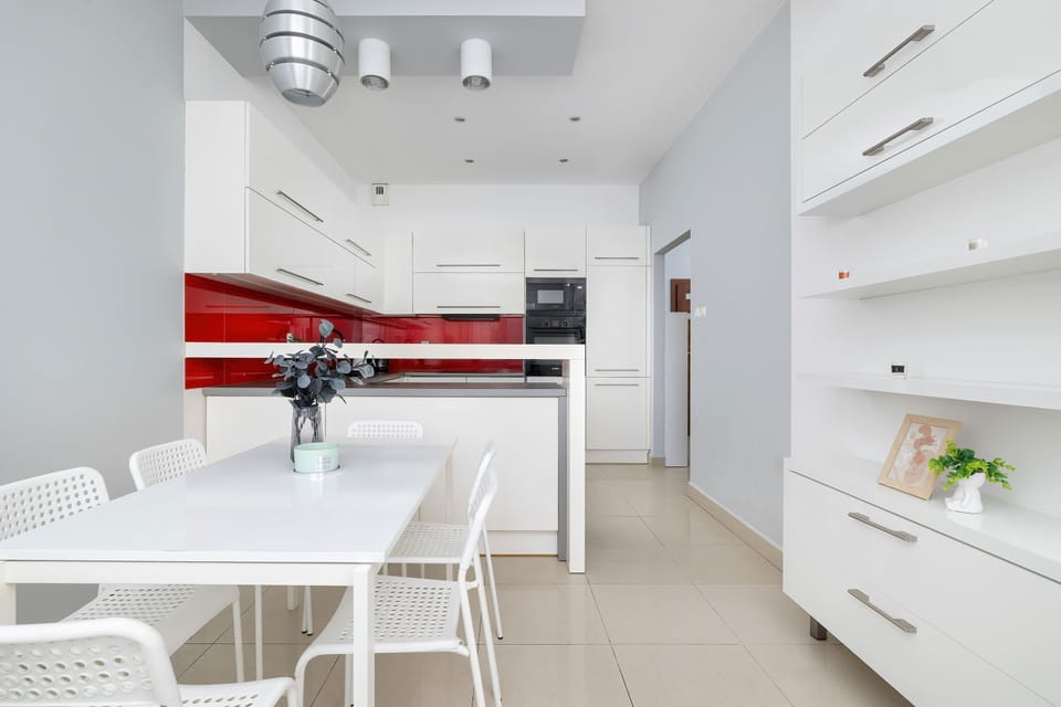 A white kitchen with red glass backsplash panels and integrated appliances. The spacious layout offers plenty of room for preparing meals.