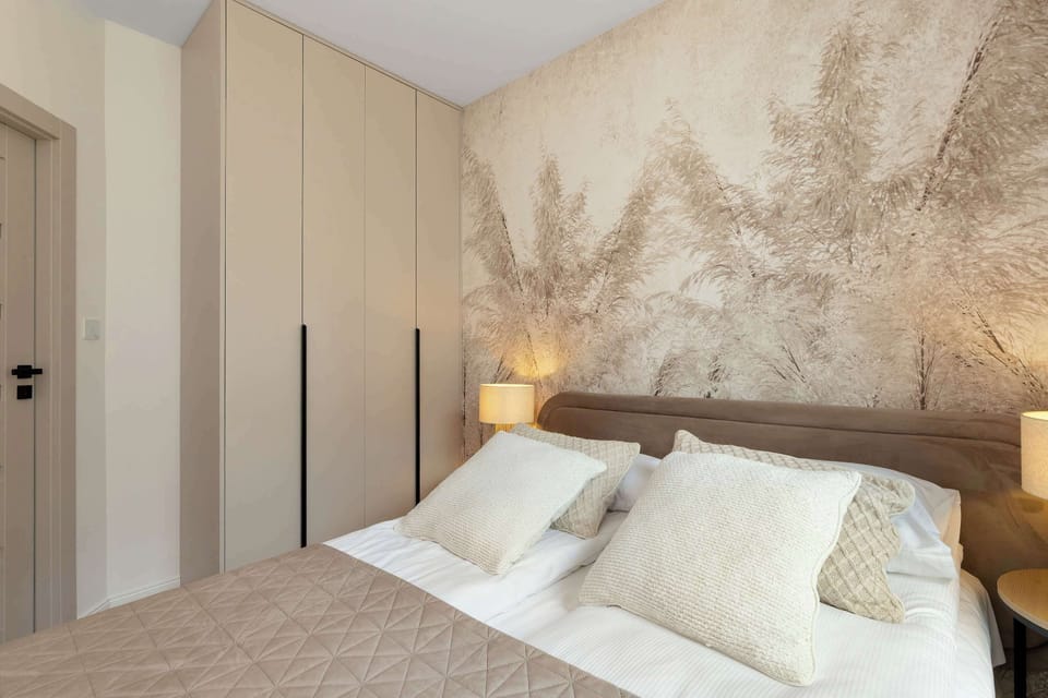 A spacious bedroom view displaying a large wardrobe with light-colored doors extending to the ceiling. The double bed is neatly made, and the prominent accent wall adds a touch of nature to the room.