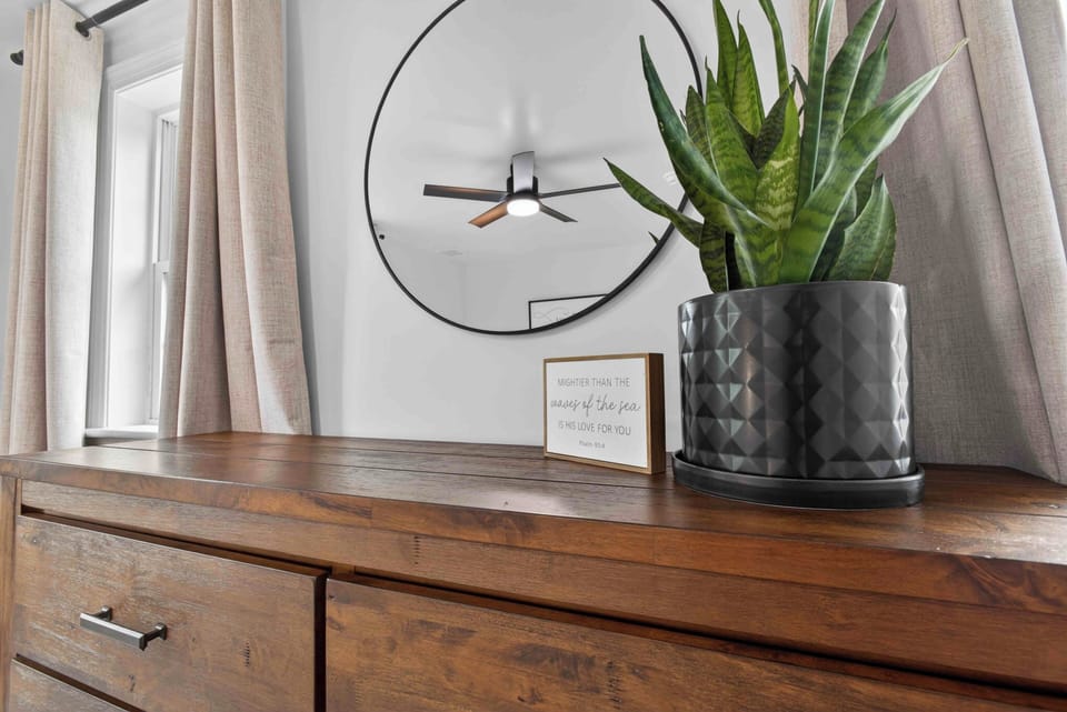 Warm wood dresser, round mirror, greenery—bright, modern comfort