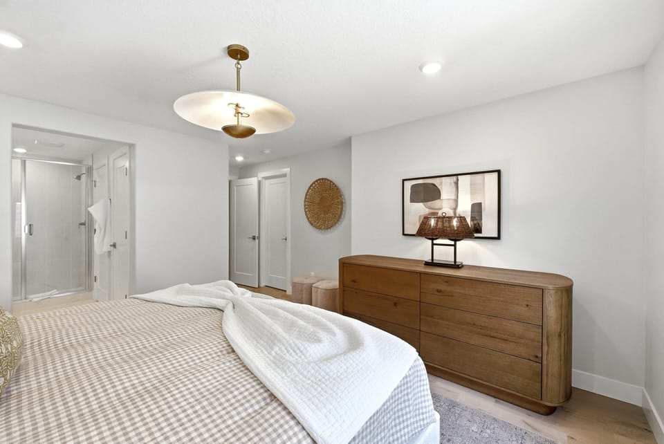 King guest suite with large dresser, warm wood accents, soft lighting, and an en suite bath nearby.