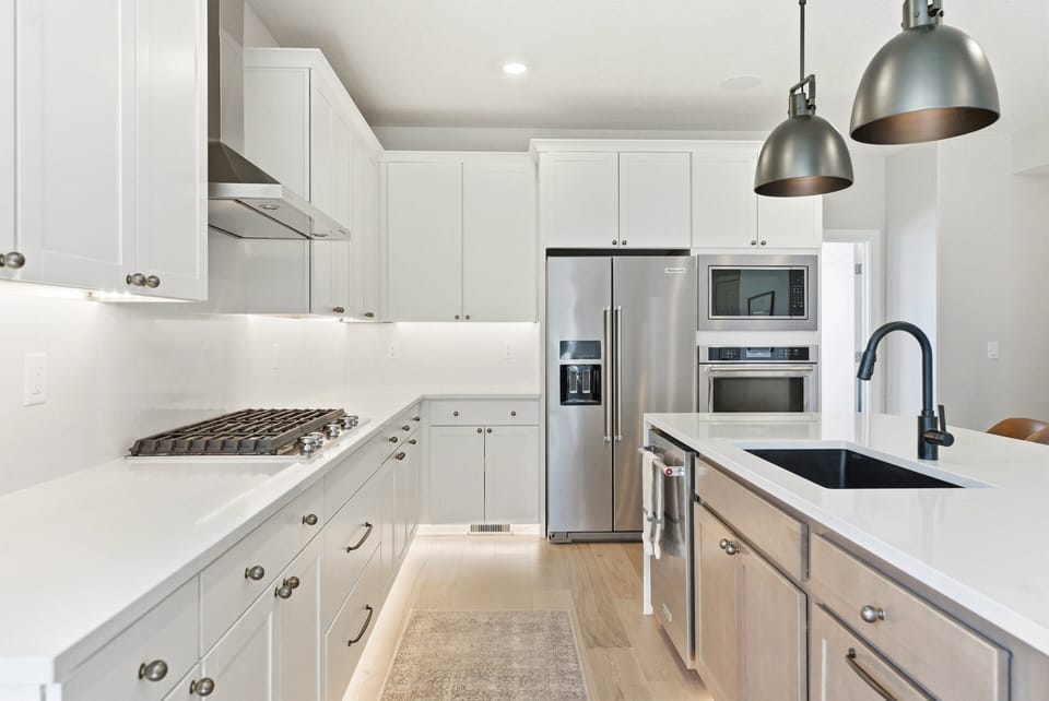 Sleek white kitchen with gas range, stainless steel appliances, farmhouse sink, and oversized island.