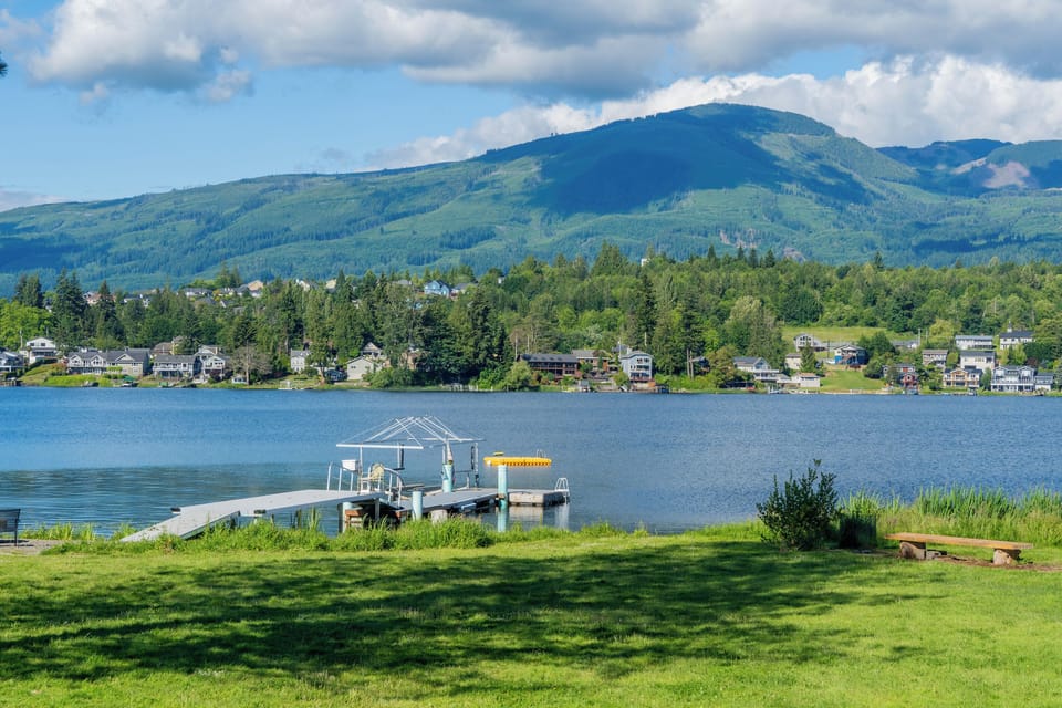 Looking out across the lake, the dock rests to the right along the shoreline. Calm water reflects the sky and surroundings, creating a peaceful, inviting scene of the lakeside setting.