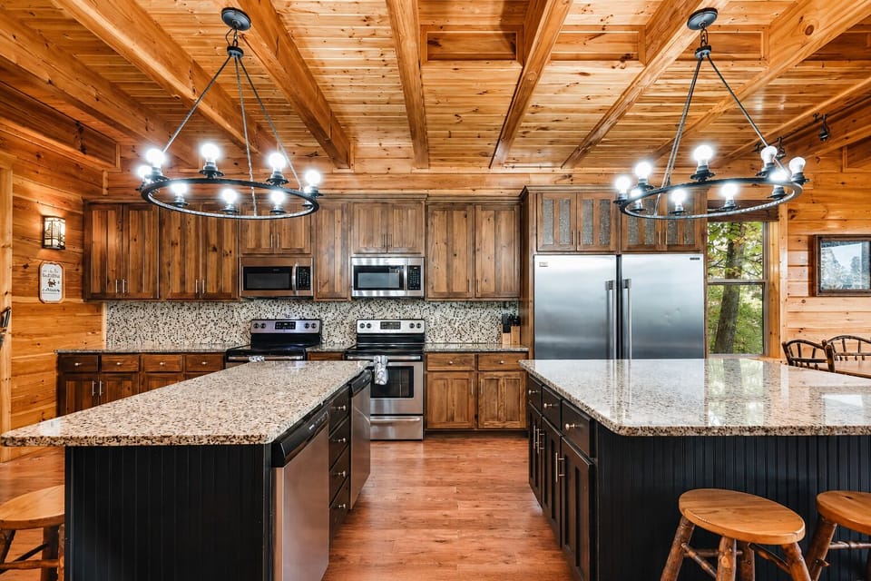 Rustic luxury kitchen featuring stainless steel refrigerator, double ovens, granite countertops, and elegant lighting in this Smoky Mountain vacation cabin.