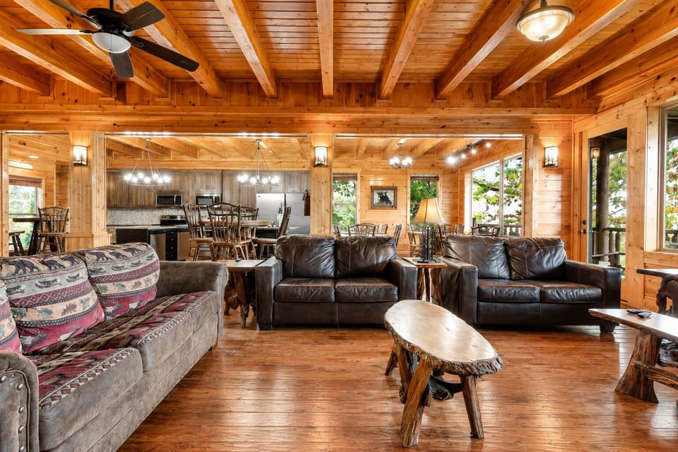 Spacious rustic living room with comfortable seating, hardwood floors, and open floor plan connecting to the kitchen and dining areas for group vacations.