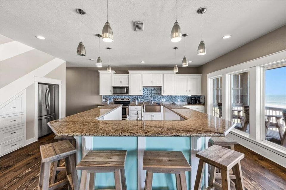 Large kitchen island with bar seating, granite countertops, and open coastal dining area perfect for entertaining guests.