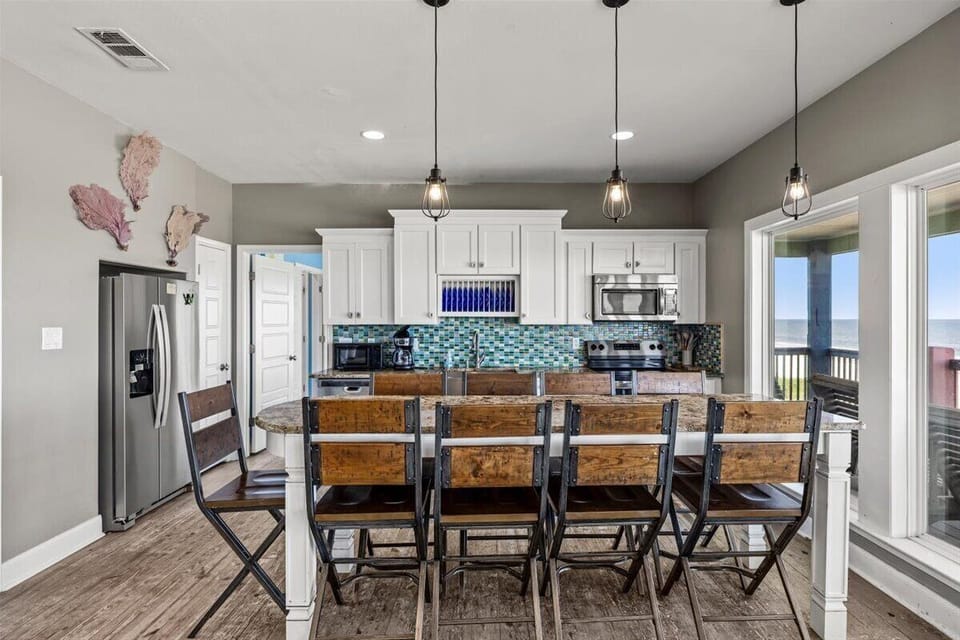 Spacious dining area with large farmhouse table, open kitchen concept, modern lighting, and seating ideal for family meals and group beach vacations.