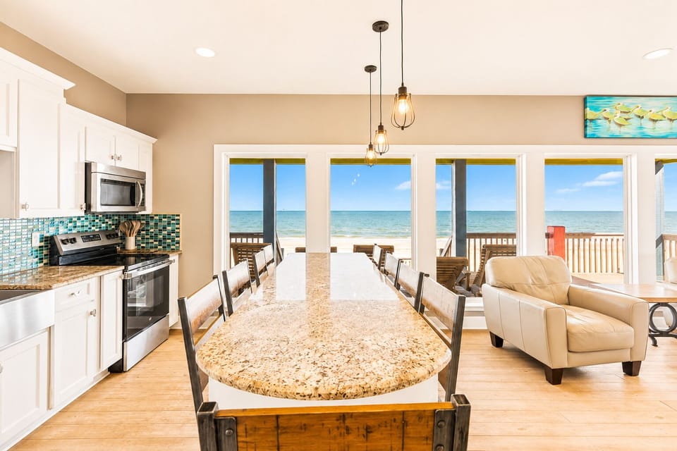 Granite dining island with pendant lights and seating, positioned beside large Gulf-view windows for ocean scenery while dining and gathering.