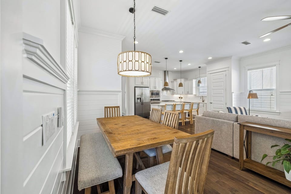 Picture yourself gathering around this inviting dining table, with sunlight streaming through large windows and a modern kitchen just steps away. The open layout and stylish lighting create the perfect setting for your morning coffee or evening meals.
