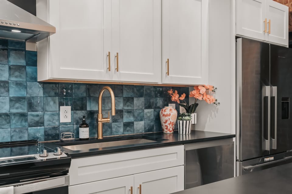 The Roxie - The kitchen features sleek stainless steel appliances, crisp white modern cabinetry, and a bold, colorful backsplash that adds a vibrant pop to the space.