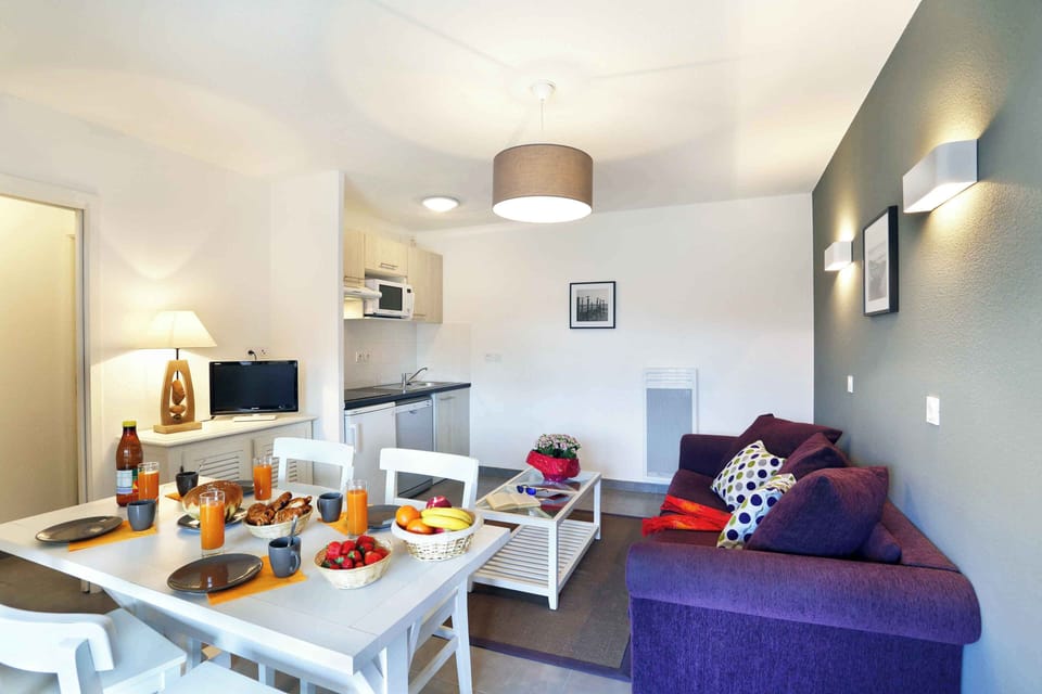 Living area with sofa bed, dining table, and direct kitchen access — kids' club runs free in July and August.