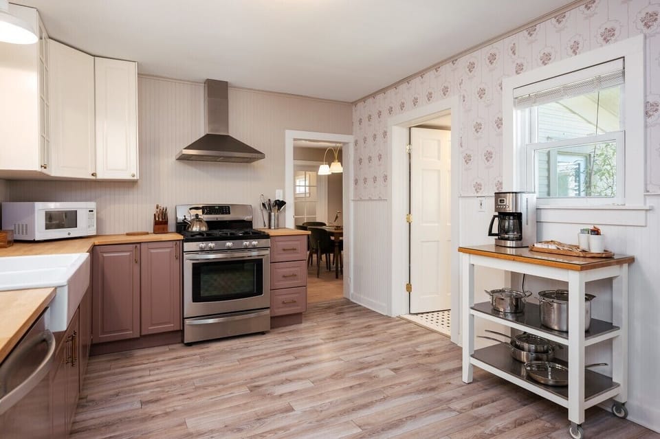 A charming vintage-meets-modern kitchen with soft mauve cabinetry, warm wood accents, and a lovely view into the dining nook. Perfectly cozy and inviting! 🍳🌸