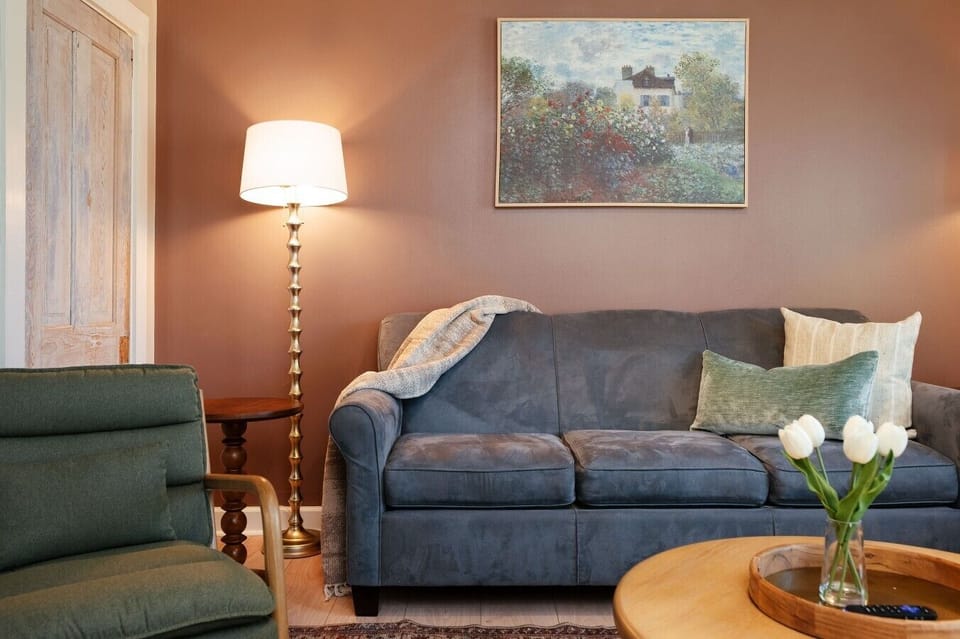 A warm and welcoming living room featuring a plush blue sofa, ambient brass lighting, and fresh tulips that bring the space to life. 🛋️💐