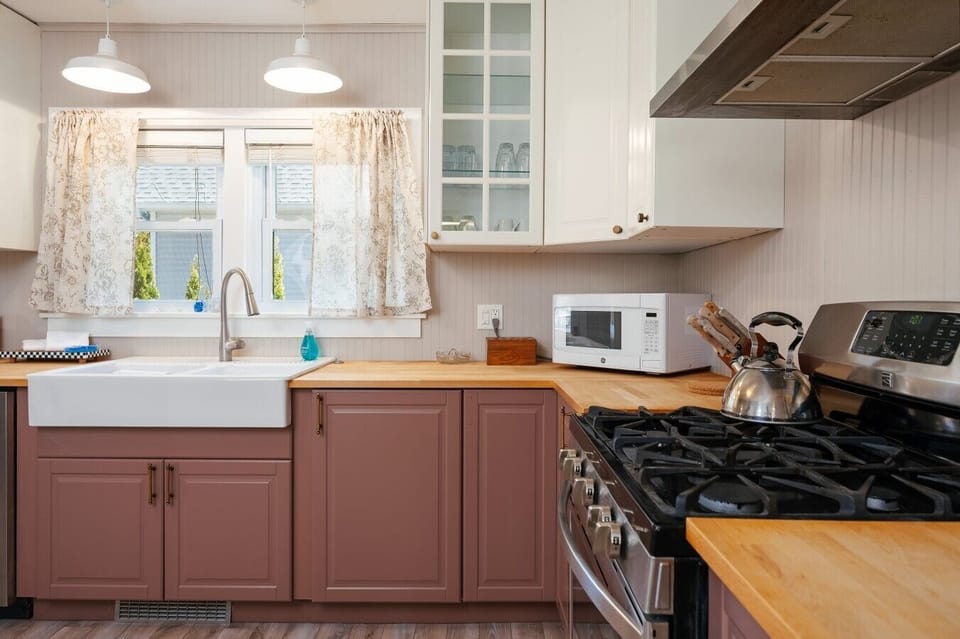 Cozy kitchen with wooden countertops, pink cabinets, a white farmhouse sink, and stainless steel appliances. 🍳🏡