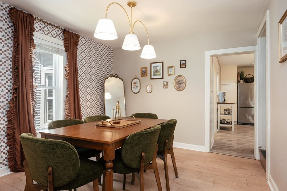 An elegant dining area with a rich wooden table, olive-green velvet chairs, and a gallery wall that makes every meal feel special. 🍽️✨