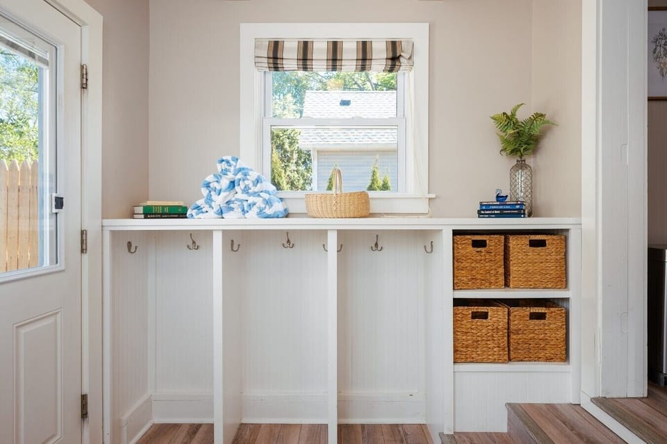 A bright, organized mudroom with built-in hooks, woven storage baskets, and a cheerful plaid window valance. 🏠🧺