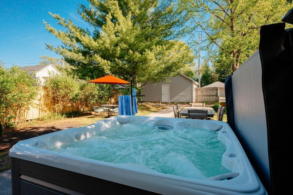 Relax and unwind in this tranquil backyard featuring a bubbling hot tub, surrounded by lush greenery and perfect for sunny days. ☀️🌳