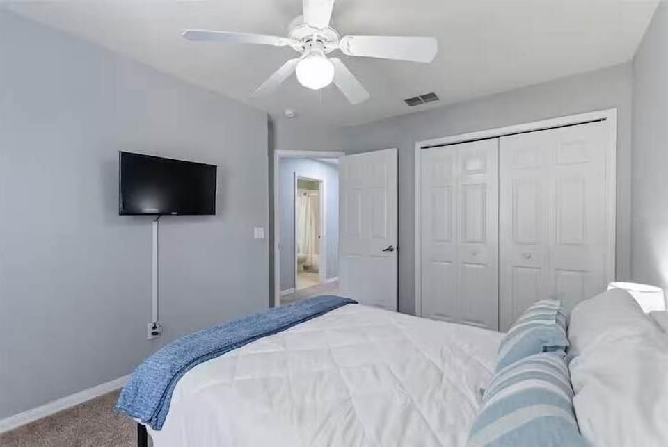 Cozy bedroom w/ a bed, wall-mounted TV & soft natural light.
