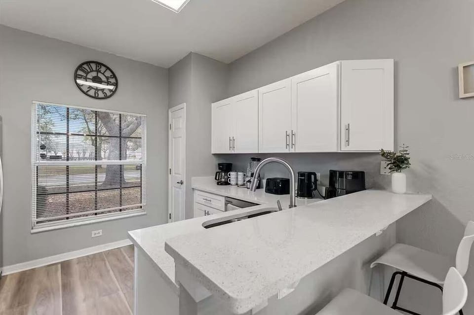 Sleek kitchen w/ white cabinetry, marble countertops & bar stool seating.
