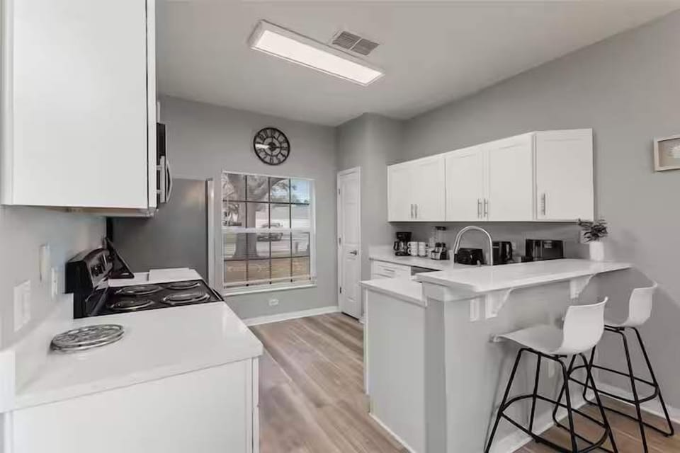 Bright kitchen w/ white cabinets, open layout & barstool seating at the counter.
