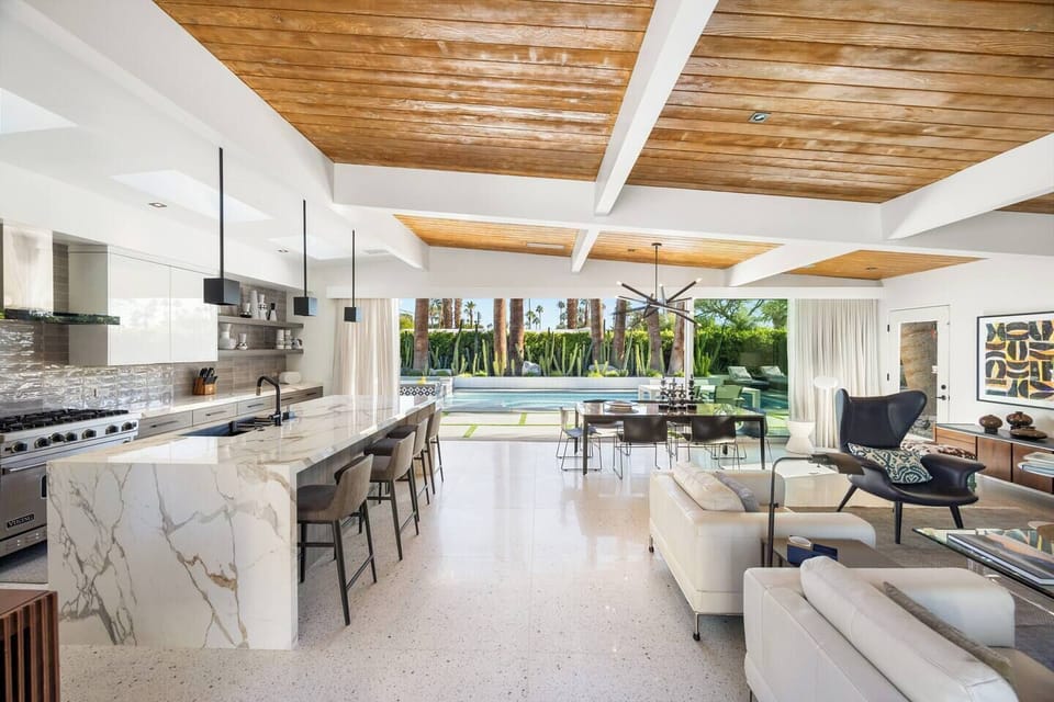 Open-concept great room flowing from gourmet kitchen to living area, all framed by walls of glass and warm wood ceilings.