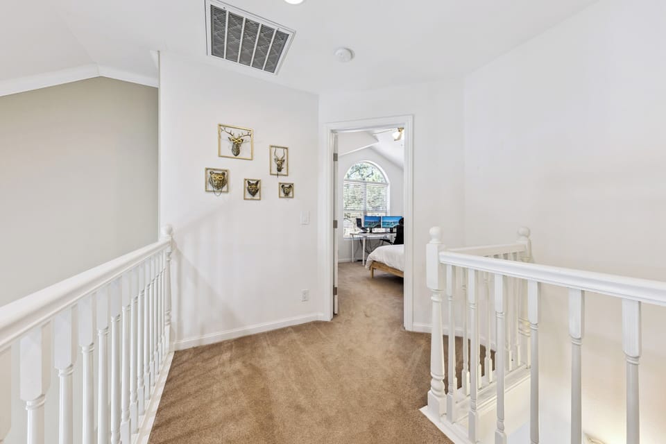 A bright upstairs hallway leads you to a peaceful bedroom retreat, framed by charming wildlife art and white banisters that add classic, homey appeal.
