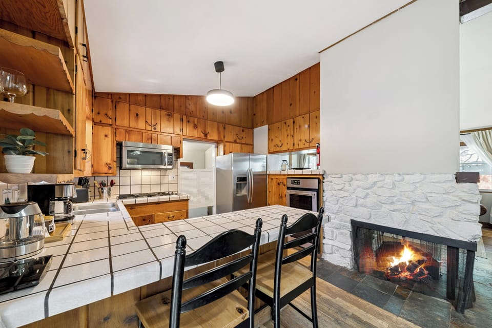 Gather around this warm, rustic kitchen featuring knotty pine cabinetry, a cozy fireplace, and a spacious tiled island—your perfect spot for home-cooked meals and memories.