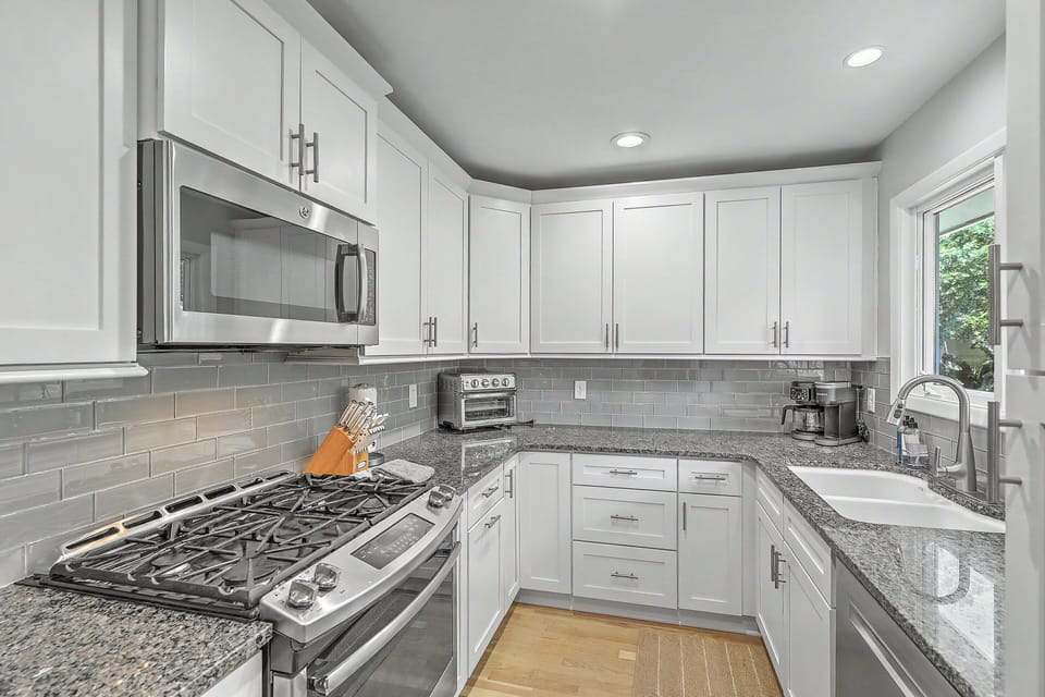 A detailed look at the cooking area showcases the premium five-burner gas stove range, a matching over-the-range microwave, a professional knife block, and an upscale grey subway tile backsplash.
