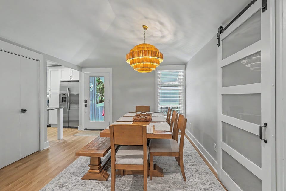 The completely remodeled dining space showcases a long wooden table set with placemats, standard chair and bench seating, and a striking tiered bamboo chandelier overhead.