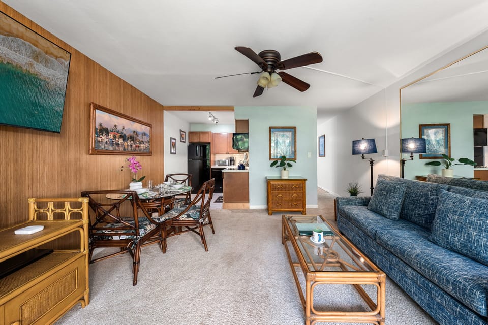 Dining table and wicker chairs gather near wood paneling, framed art adding warmth to the space.