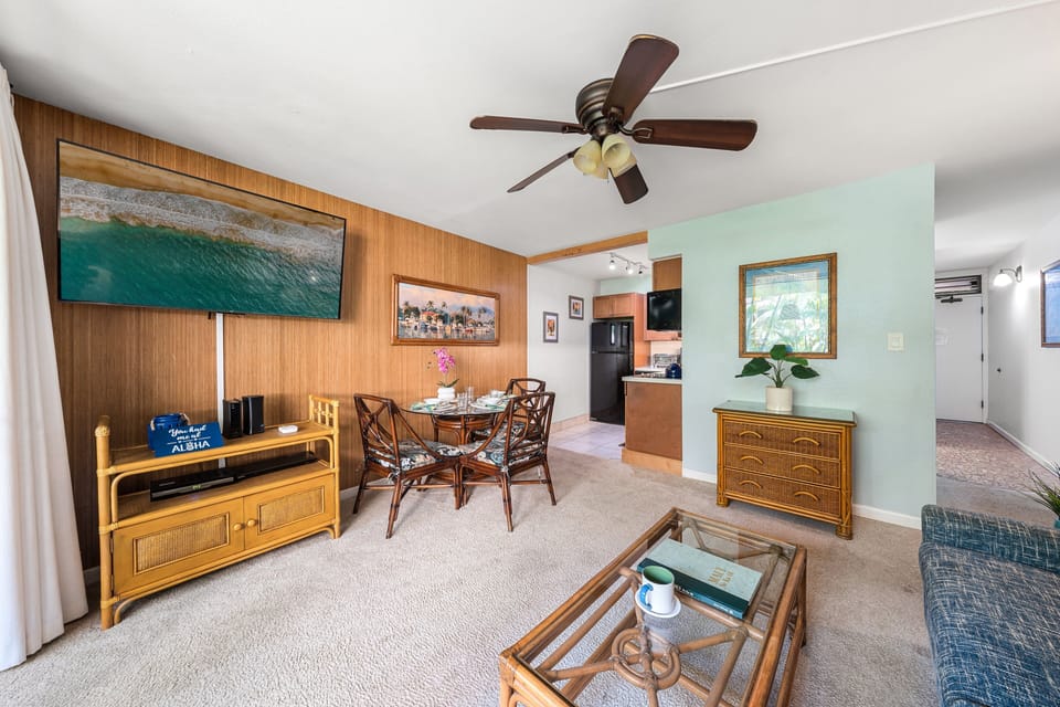 Open plan flows with coordinated furniture and ocean art, ceiling fan spinning above the scene.