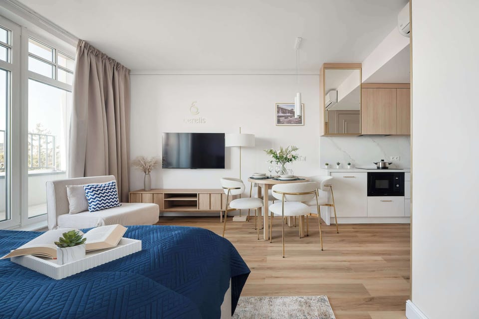 The open-plan layout combines a lounge area with a blue velvet sofa and a small dining nook. The white walls and light wood floors maintain a bright and spacious feel throughout.
