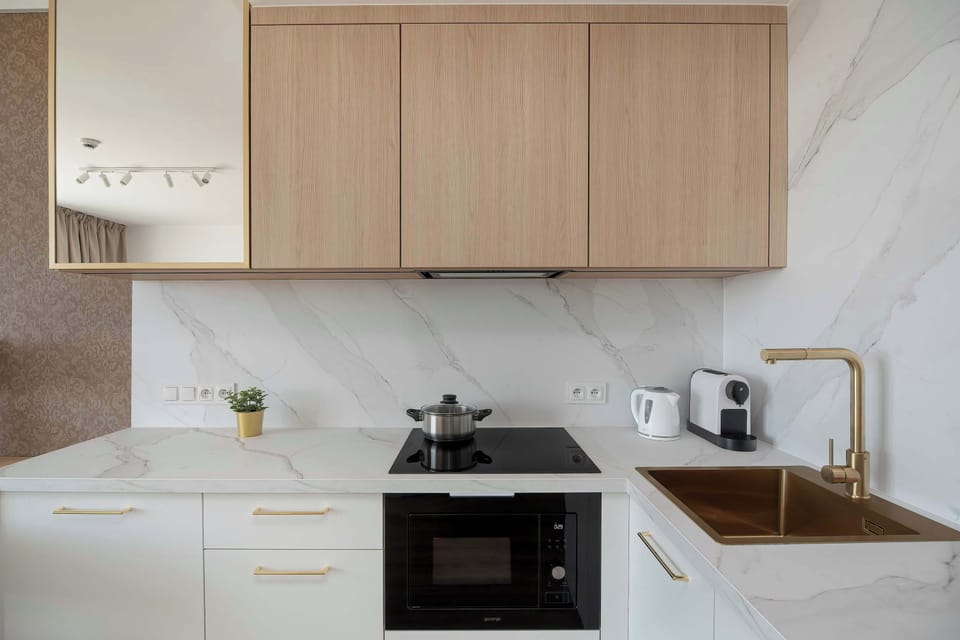 A detail shot of the kitchenette reveals a black induction cooktop and a gold-toned sink. The marble-patterned backsplash provides a high-end finish to the workspace.