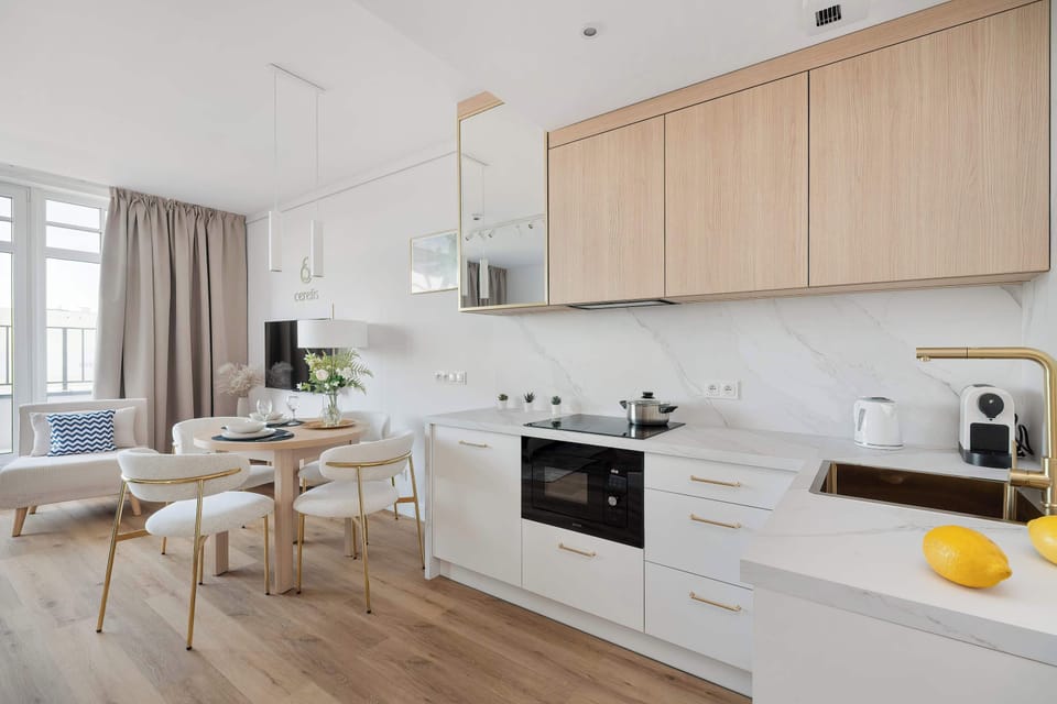 This wide shot captures the entire living and cooking zone, emphasizing the integrated design. The wooden accents of the cabinets and furniture bring warmth to the white interior.