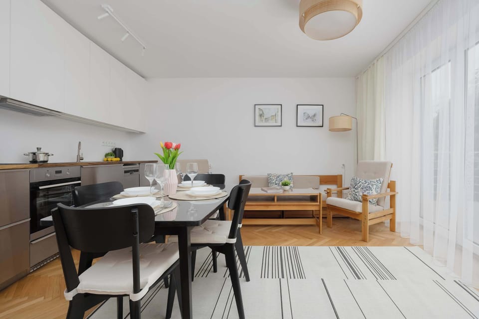 A spacious dining area with a black table set placed beside the kitchen and lounge space. Large windows and bright interiors make the room feel open and inviting.