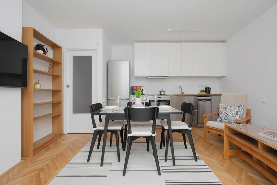 A stylish kitchen and dining space with wooden shelving, modern lighting, and sleek white cabinets. The combination of natural wood and light tones creates a modern aesthetic.
