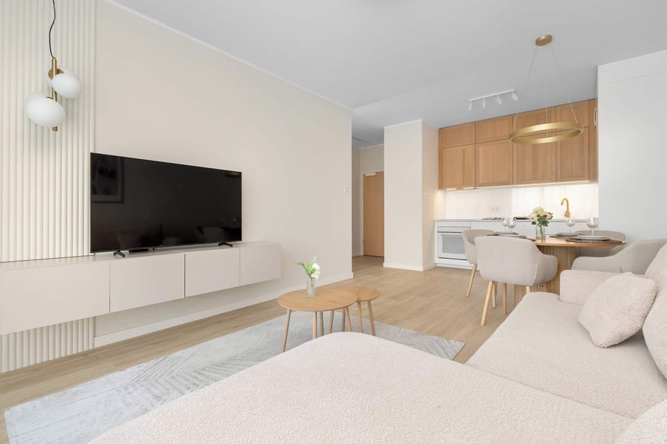 Another view of the living room with a wall-mounted TV and open-plan kitchenette.