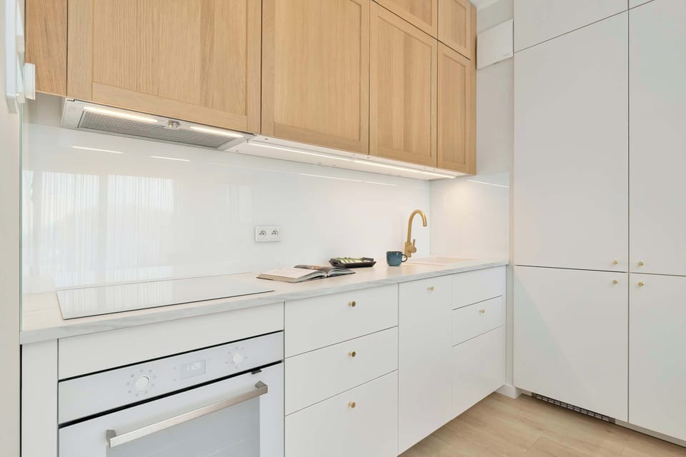 A modern kitchenette with sleek white cabinets, wooden accents, and built-in appliances.