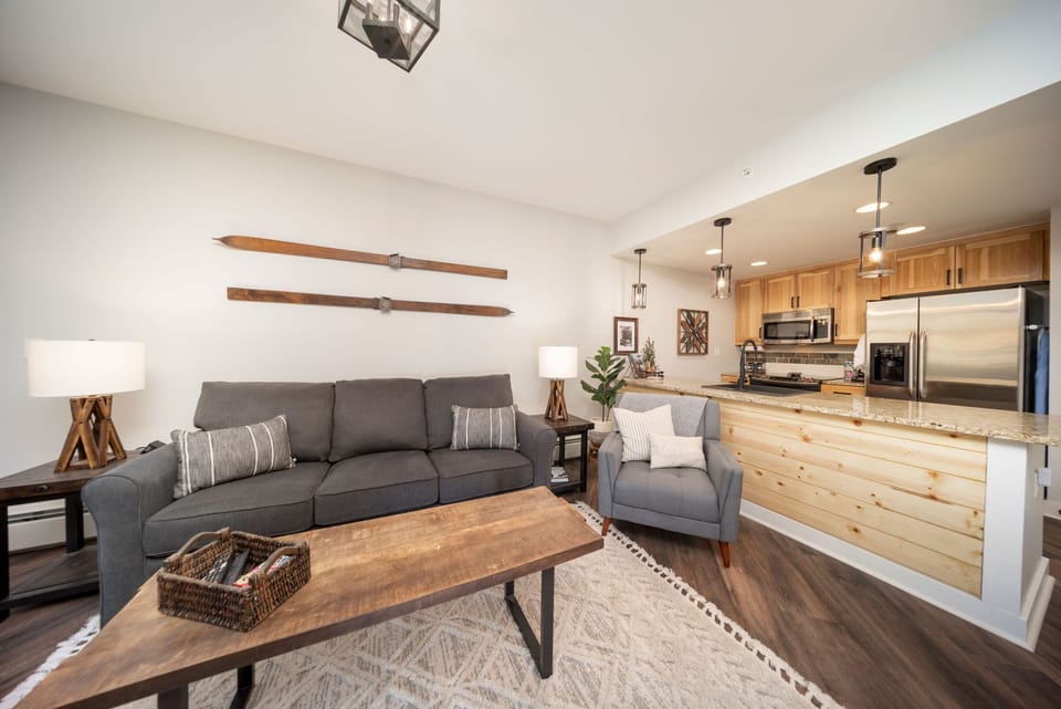 Unwind in your inviting living space with soft seating and mountain-inspired décor, flowing seamlessly into a fully-equipped kitchen perfect for preparing meals together.