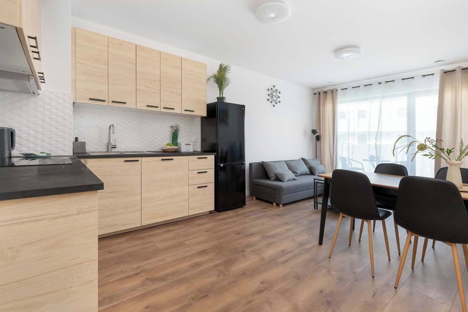 An open-plan living area showing the transition from the light wood kitchen cabinetry to the dining and sitting area. The layout is functional and maximizes the available square footage.