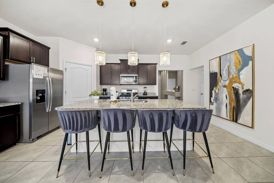 Gather at the spacious kitchen island with stylish navy bar stools, ideal for casual dining or morning coffee. Experience the blend of rich dark cabinetry and a bright layout, enhanced by modern pendant lights and vibrant artwork.