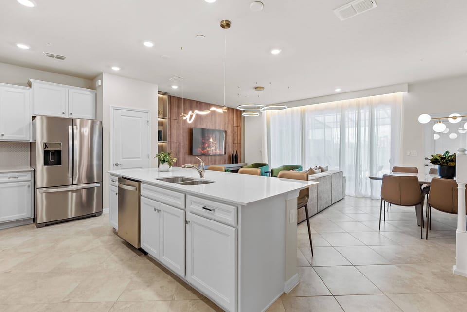 Welcome to a modern kitchen featuring sleek white cabinetry and a spacious island, perfect for meal prep or casual dining. Large windows bathe the room in natural light, enhancing the warm wood accents and cozy atmosphere.