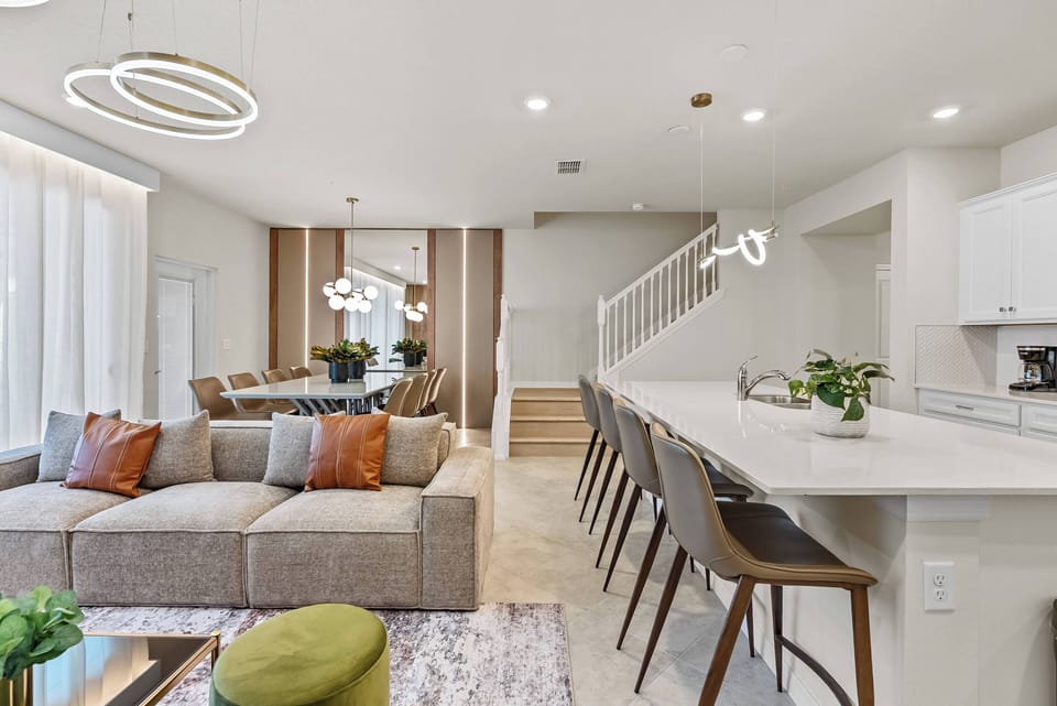 Unwind in the spacious contemporary living area with a cozy sectional sofa and colorful pillows. The stylish kitchen island with modern bar stools is perfect for casual gatherings, complemented by inviting warm lighting for.