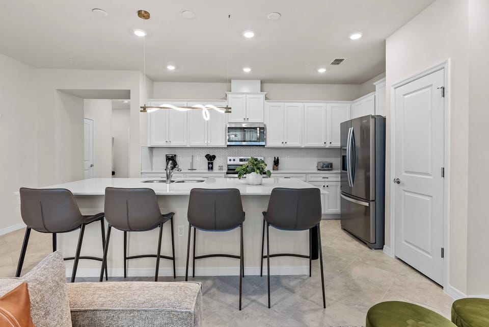 Welcome to this modern kitchen featuring sleek white cabinets and a spacious island with stylish bar stools, perfect for casual gatherings.