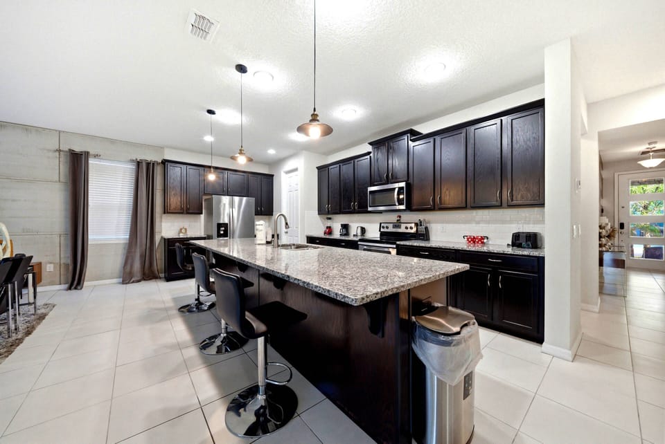 Enjoy culinary delights in this inviting kitchen, complete with rich dark cabinetry and a stunning granite island ideal for gatherings. Modern appliances and sleek bar stools make it a perfect space for cooking and entertaining.