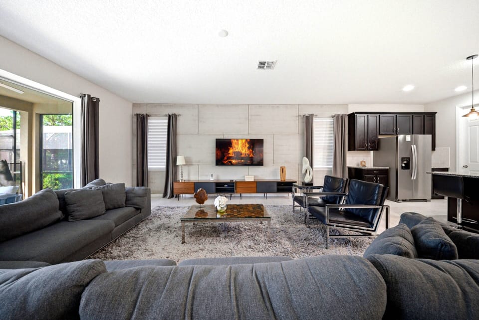 Unwind in the spacious living area with soft gray sofas and large windows that fill the room with natural light. Enjoy the modern decor, sleek coffee table, and the cozy fireplace, perfect for warm evening gatherings.