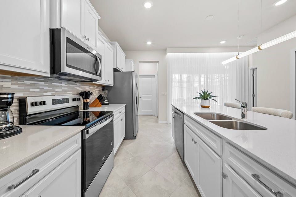 Bright and functional, this kitchen features sleek white cabinetry paired with modern stainless steel appliances. The generous counter space invites culinary creativity, while abundant natural light enhances the airy atmosphere.