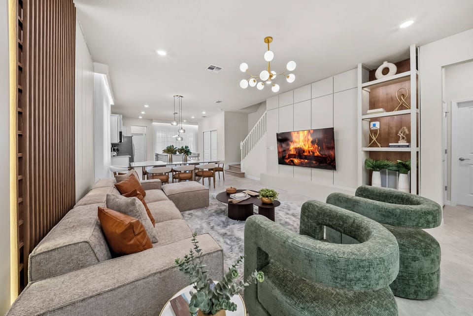 Enjoy a stylish living room with cozy gray sofas and vibrant green chairs, blending comfort and chic design. A contemporary light fixture and large TV create a relaxing space perfect for connection with friends and family.